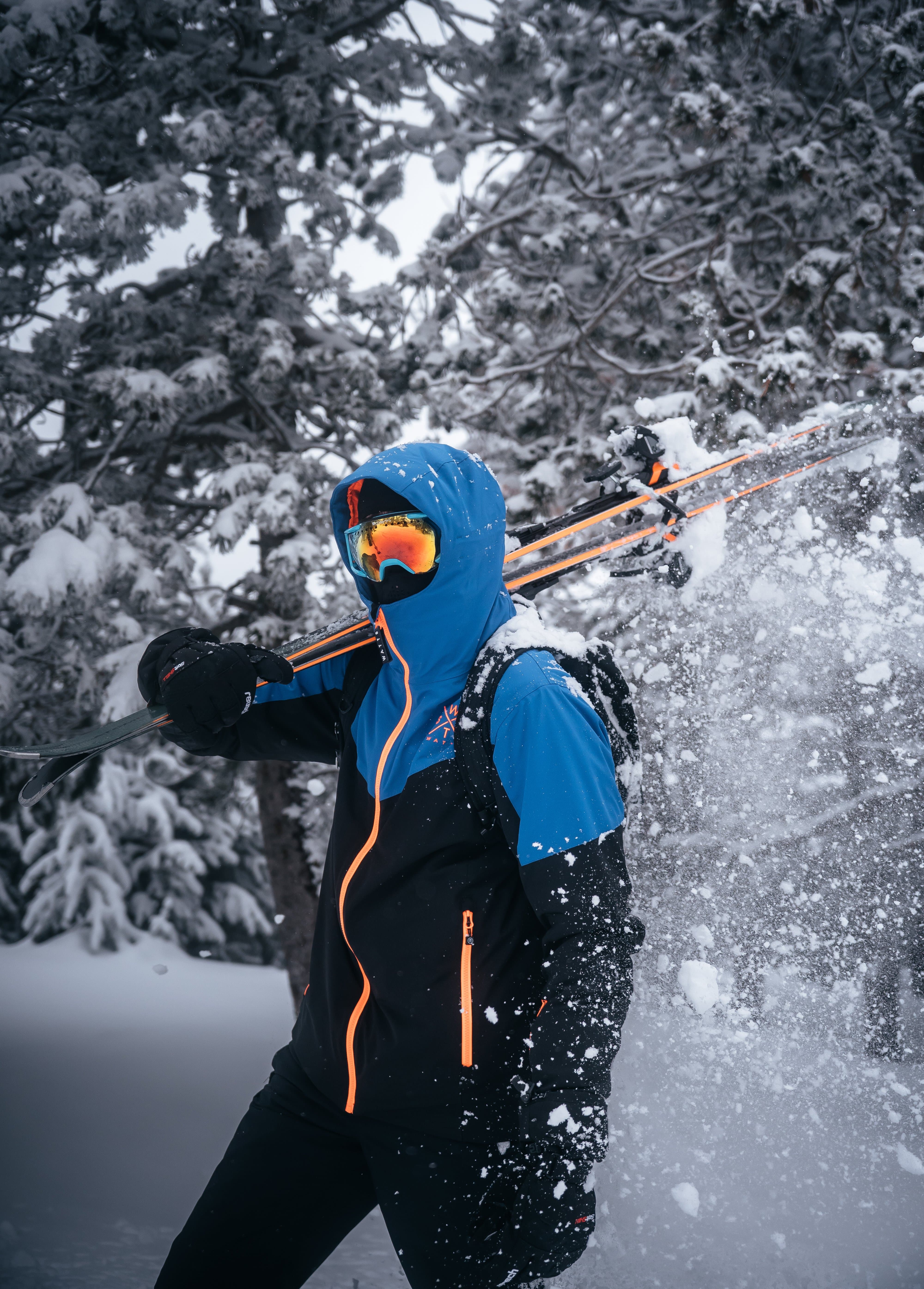 Skieur en veste bleue marchant dans une forêt enneigée des Pyrénées avec des skis sur l’épaule